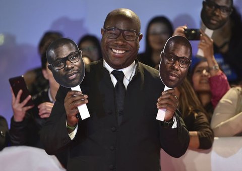 Director Steve McQueen poses with paper cutouts of his face as he attends the premiere for 