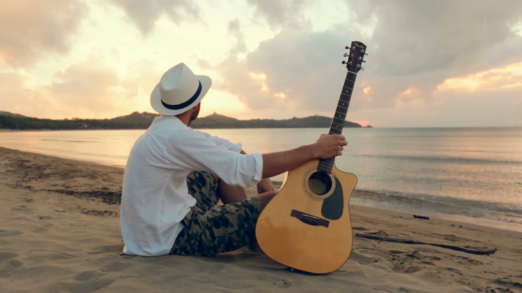Young Beautiful Man Plays Guitar Outdoor At Beach
